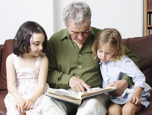 Image of older man viewing photo album with grandchildren