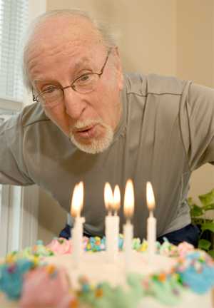Photo: Elderly man blowing out candles on a cake 
