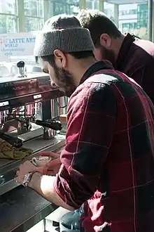 A man makes coffee in at a coffee shop.  Sunlight streams through the windows.