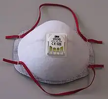 A white cup-type filtering facepiece respirator with an exhalation valve and red head and neck straps