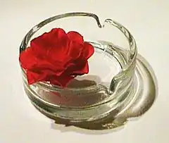 Clear ashtray with a red rose in it.