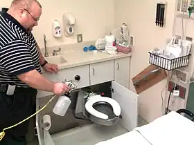 A man using a spray bottle to clean a hospital toilet