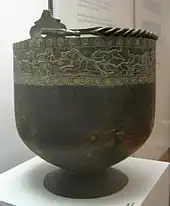 Large black bowl-shaped bucket on a stand. The bucket has incrustation around its top.