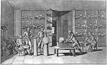 Black and white engraving of Lavoisier's laboratory, man seated at left with a tube attached to his mouth, man at center conducting experiment, woman seated at right drawing, other people visible