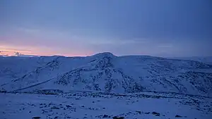 Snow-covered mountains. The whole view appears tinted blue, aide from a faint pink glow on the left of the horizon, which is the sun at its peak.