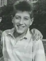 A teenage male with the hand of another resting on his left shoulder smiling for the camera