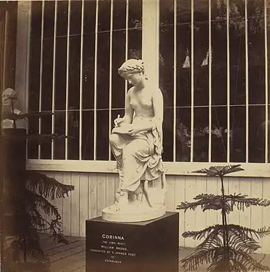 A statue of a seated woman, nude from the waist up, with a lyre at her feet