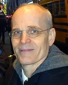 Close-up photograph of a thin bespectacled man, mostly bald with short gray hair around