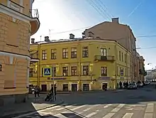 A yellow three-story corner building with a balcony on the third floor of the corner façade.