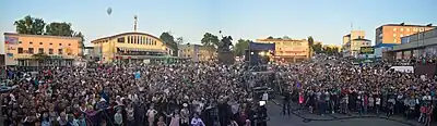 Large crowd standing outdoors in the street and watching an event out-of-frame