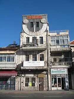 A narrow, four-story-high building with a large sundial on the fourth floor