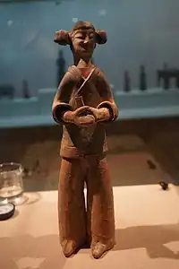 Colored standing female figurine with double hair buns, holding a hu (ritual baton)