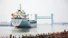 a ship going up a river towards a lifted vertical-lift bridge in the background