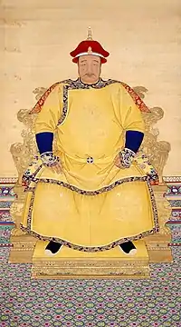 Full-face painted portrait of a corpulent man with a thin mustachio wearing a red hat and a multi-layered yellow robe with dragon decorations, and sitting on a throne mounted on a low podium.
