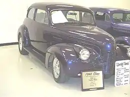 '40 Chev custom with painted grille, small front turn signals, custom door mirror, and frenched radio aerial. This vehicle has a non-stock one-piece windshield.