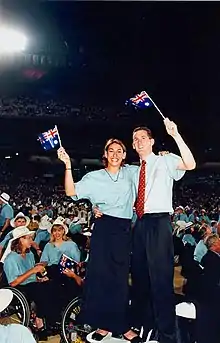 Two people standing on folding chairs and holding small Australian flags
