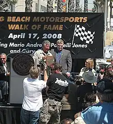 A ceremony where a retired racing driver receives a plaque from a city official