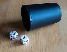 Two six-sided dice and a cup on a wooden surface. In the photograph, the dice are showing the values 6 and 3, which has an odd sum (9). In the game Chō-han, players who bet on 'han' (odd) would win their bets.