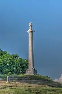 Photo shows a tall, white column, with a torch at the top.