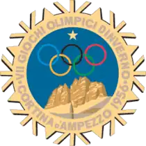 A stylized snowflake with the Olympic rings, a star and mountains. Surrounding the perimeter of the snowflake are the words, "VII Giochi Olimpici d'Inverno, Cortina d'Ampezzo 1956"