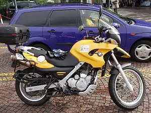 Yellow BMW F650GS fitted with optional top box and parked next to a blue car