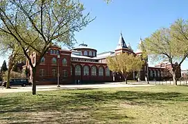 A long brick building is partial obscured by three trees. There is a central entranceway flanked by two towers, and a rotunda behind the entrance.