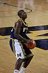 A basketball player in a dark blue uniform is eying a shot with the basketball in his hands at his waist.