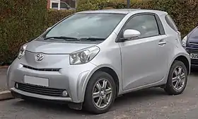 Front-three-quarter view of a three-door car with a one-box body style whose passenger door spans almost the entire distance between the front and rear wheel arches; the car is fitted with alloy wheels, flush headlights, front foglamps, and door mirrors with integrated turning indicator lights.