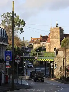A green railway bridge over the road with a church behind