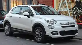 White car paked at roadside with a backdrop of shops