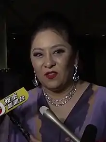 Chen dressed in purple being interviewed with microphones at night.