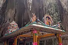 Four-pillared structure with religious statues on the roof in front of a rock wall inside the cave.