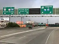 A split in a multi-lane freeway under construction with three green overhead signs. The left sign reads west Route 139 to U.S. Route 1 and 9 Interstate 280 Pulaski Skyway with two downward arrows, the middle sign reads Kennedy Boulevard Jersey City with two downward arrows, and the right sign reads New Jersey Turnpike Interstate 78 to Interstate 95 with two arrows pointing to the upper right.