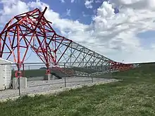 Red and white radio tower crumpled and bent at the base, the rest of the tower collapsed all the way to the ground.