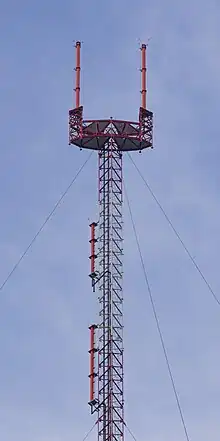 A tall antenna with a goalpost-shaped appendage with two red antennas. Two antennas are mounted lower on the mast.
