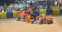 A race car being removed from the circuit after an accident by five people wearing orange for visibility