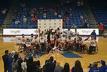 A wheelchair basketball team posed for photographs while celebrating a championship with the trophy
