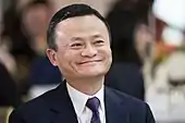 Jack Ma wearing a navy blue suit and matching patterned tie with a white shirt while smiling.