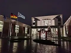 The Federal Chancellery in Berlin during the presidency, with a flag featuring the logo of the council presidency flying in front of the building, next to a flag of Germany and one of Europe