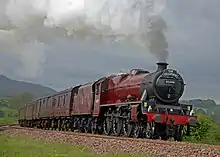 a steam locomotive painted maroon with a black smoke-box and chimney going round a curve in moorland scenery with coaches behind