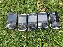 5 mobile phones that have been shown on grass and are being sold at a car boot sale.