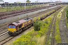 A diesel freight locomotive pulling wagons of continuously welded rail past stationary freight wagons