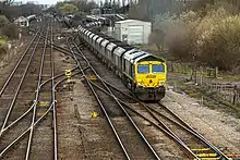 A diesel locomotive hauling empty coal wagons on a four-track railway with sidings in the distance