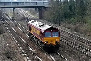 A diesel locomotive on a four-track section of line, with an overbridge behind