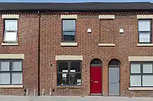 A colour photo of a red-bricked house with boarded up windows and doors