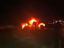 At night, armoured car sitting engulfed in flames in the middle of a road