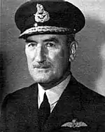 Head-and-shoulders portrait of man in dark uniform with peaked cap and pilot's wings on left-breast pocket