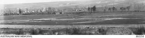 A black and white photograph of a landscape with a railway embankment in the middle distance, behind which is a village