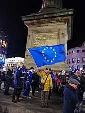 People standing around the base of the monument. One carries a European Union flag.