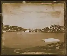  a sepia toned photographic view of four ships in the distance sailing through a channel.